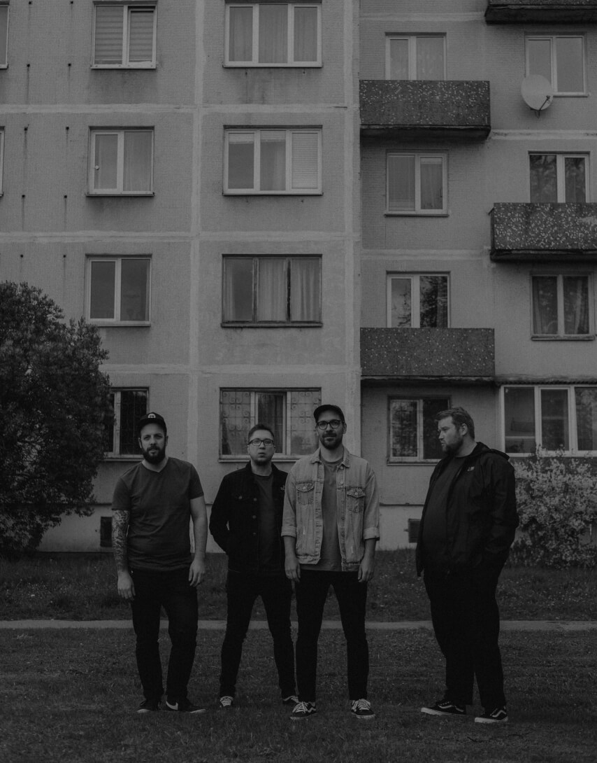 Black and white image of the four Have No Heroes punk rock band members standing in front a  soviet 9 storey building